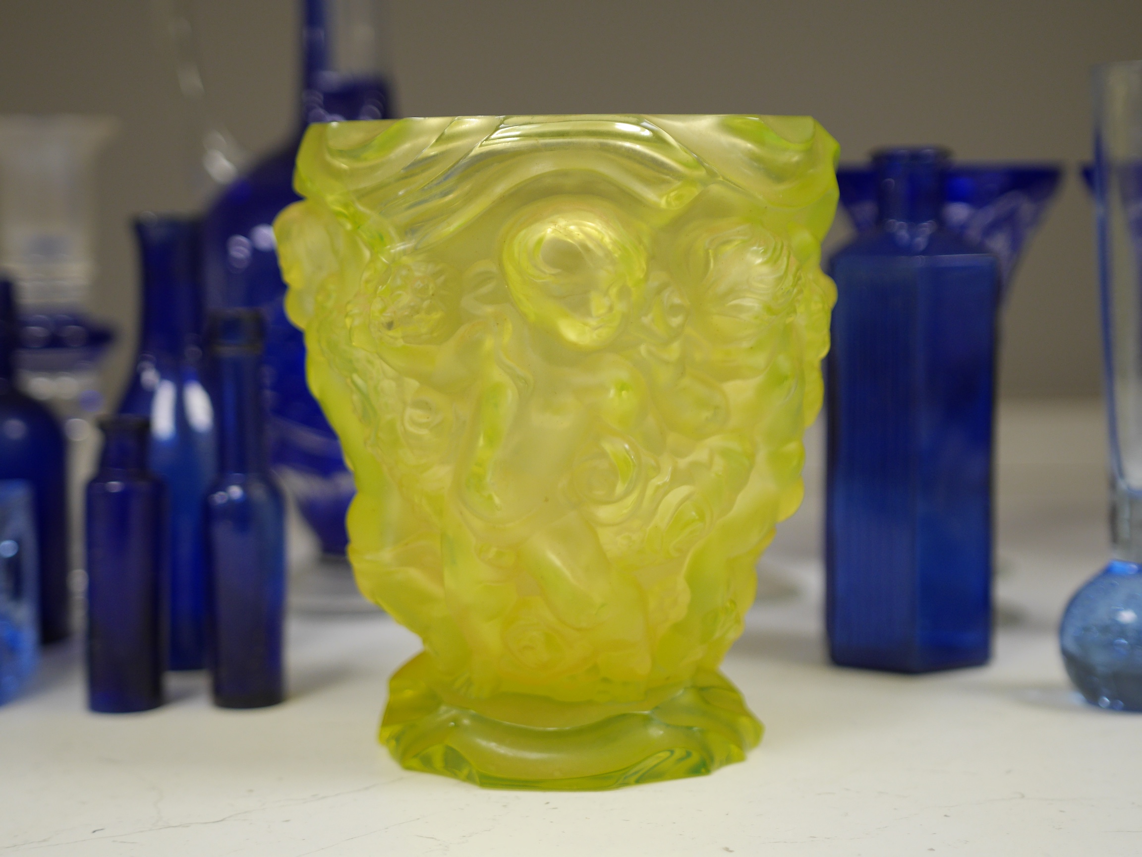 A yellow glass putti decorated vase, a blue glass decanter and other blue glassware, vase 18cm high. Condition. - one glass broken